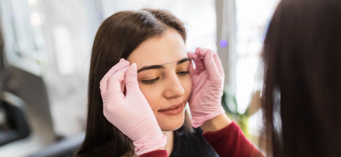 Female master checks the contour of the eyebrows with thread
